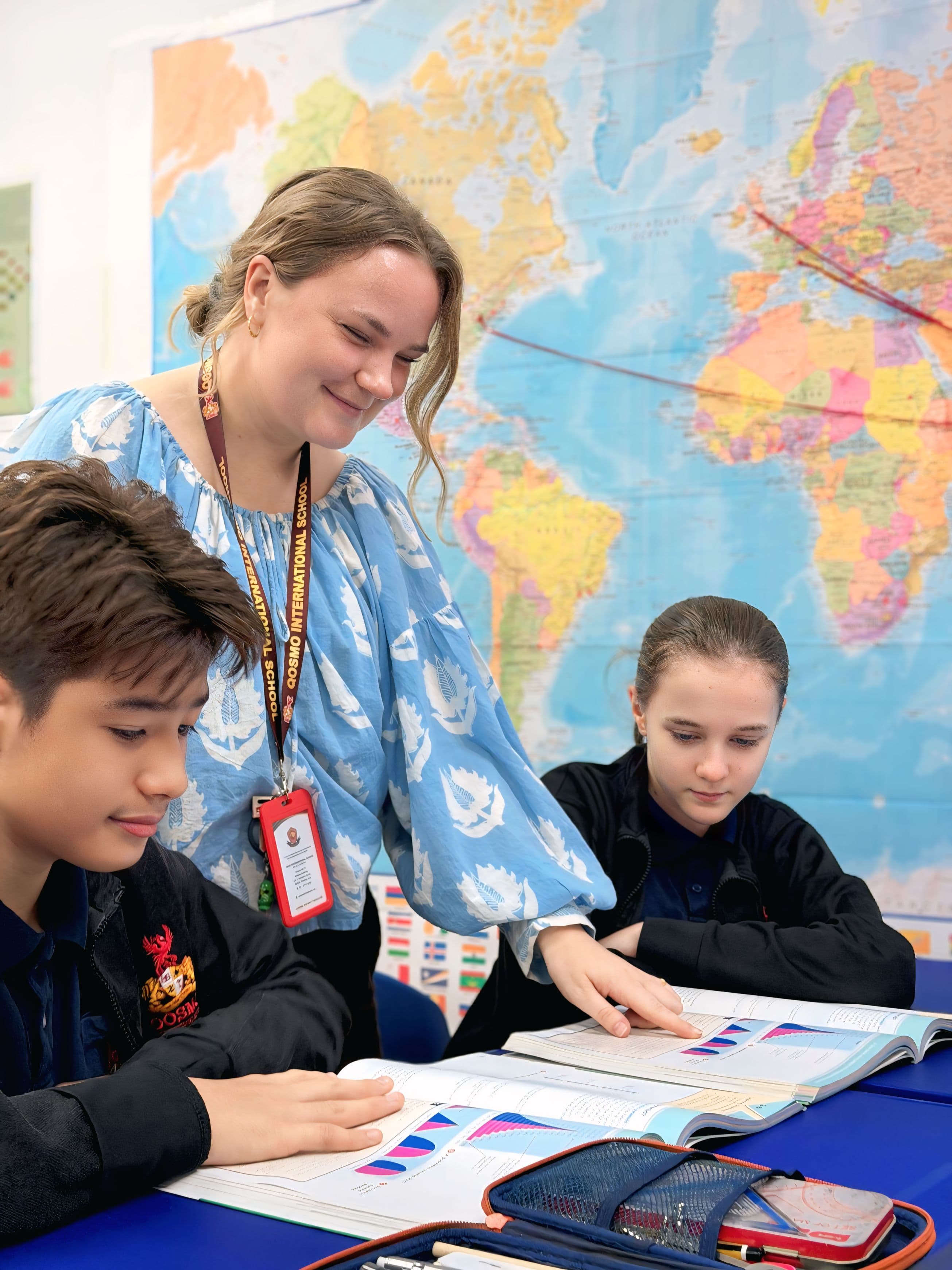 A teacher guiding two students through a classroom activity at Qosmo International School.