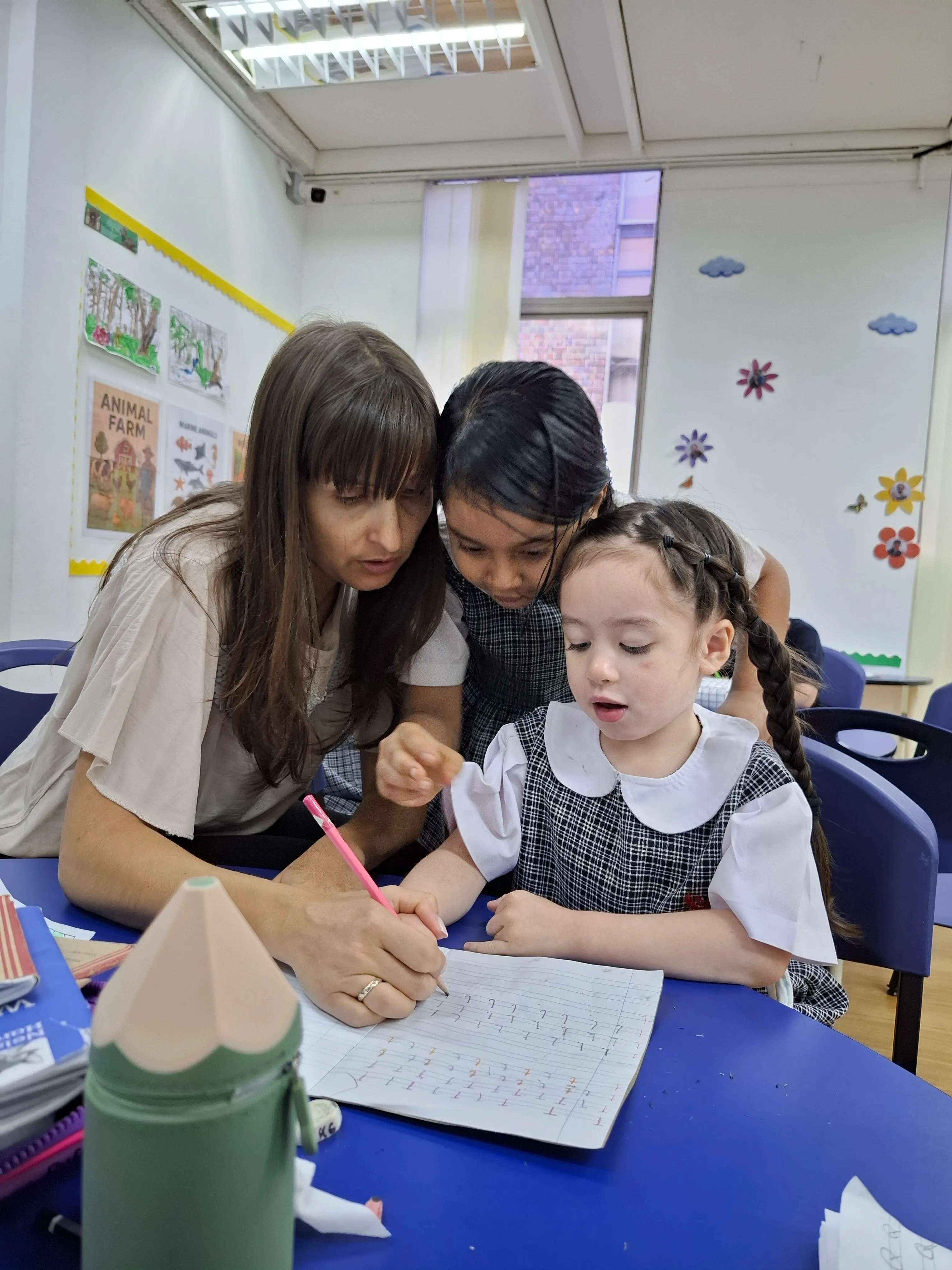 A teacher guiding children in Qosmo's Early Years programme during a classroom writing activity.